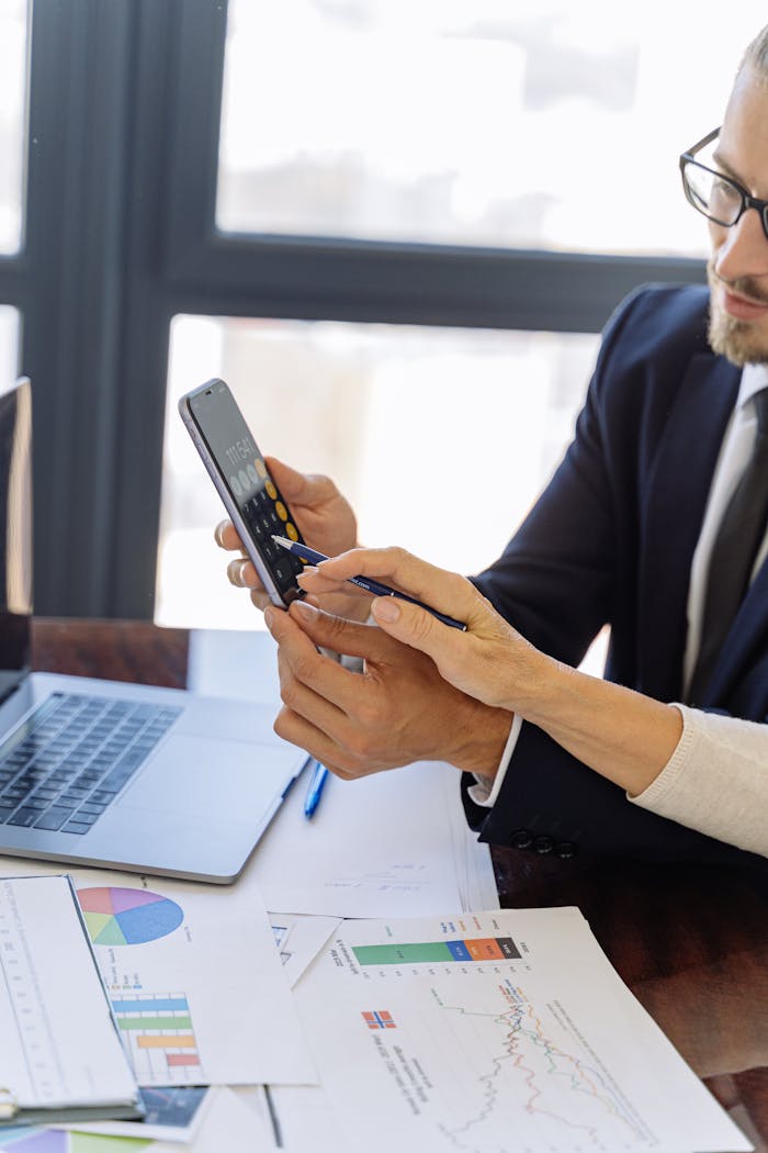 Crafting Captivating Headlines: Your awesome post title goes here Business professionals reviewing financial reports on a smartphone at a desk with papers and a laptop in an office setting.